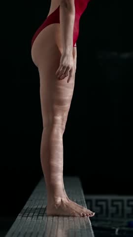 Athlete in red swimsuit poised on diving board then cutting through dark pool water, capturing the focused transition from tense stillness to powerful motion