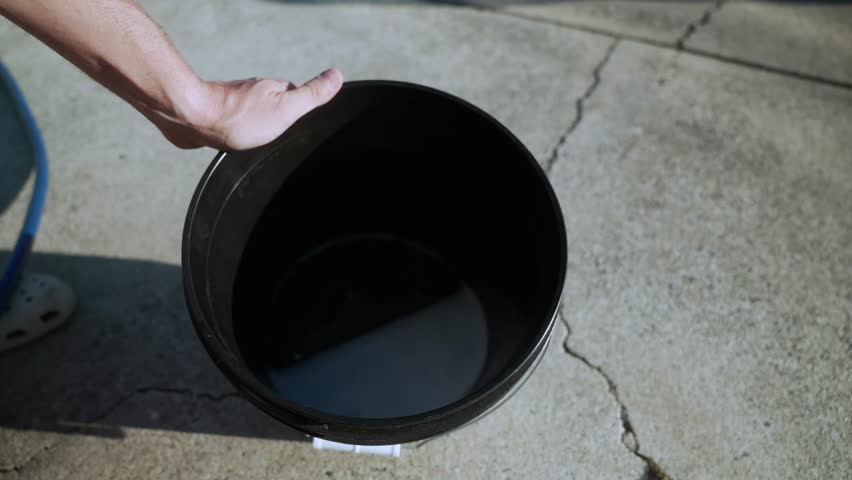 Close-up of water spraying into a soap bucket with a hose on outdoor pavement