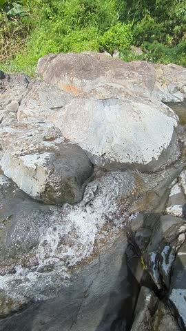 Lush, verdant mountainside with a clear blue sky and wispy clouds, featuring rough, textured rocks in the foreground with a gentle stream flowing. with intricate details.