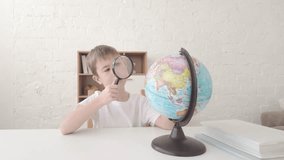 Boy studies globe with magnifying glass at desk in bright classroom, looking closely at map details for school learning - Powered by Shutterstock - Get 15% off with code: PIKWIZARD15