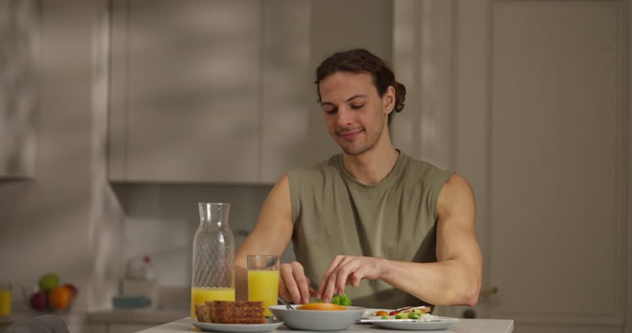 Enjoying a nutritious breakfast in a well-lit kitchen, a man prepares fresh vegetables and drinks orange juice