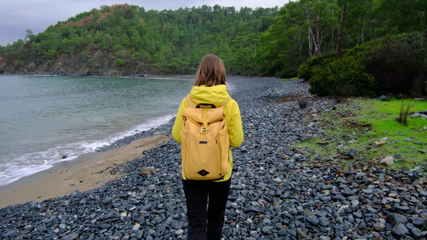 Young woman walks alone along cold Turkish coast. Windy, cloudy weather, peaceful solitude and gentle connection with nature by stormy sea.