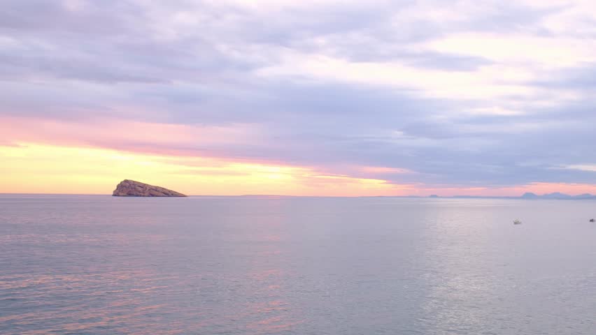 Sunset view over Cala Tio Ximo and Benidorm island. Tranquil winter sea, soft sunset glow, peaceful view of small island near Benidorm. Quiet natural beauty, no people, only sea and sky.
