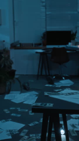 Vertical shot of disordered office space after break-in, with scattered documents and money across floor in dim lighting