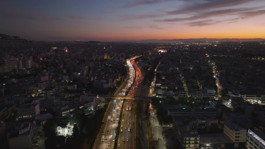 A twilight aerial view of Athens capturing the glowing horizon and the flowing traffic lights along the national road, blending city energy with the soft evening sky.