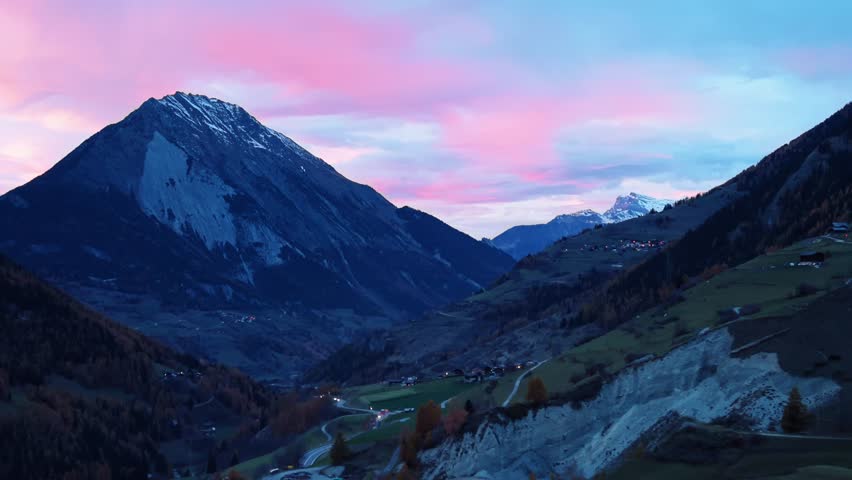 Aerial view of the valley with mountain peaks silhouetted against a vibrant pink and blue sky at sunset, creating a serene and picturesque landscape, Liddes, Switzerland.