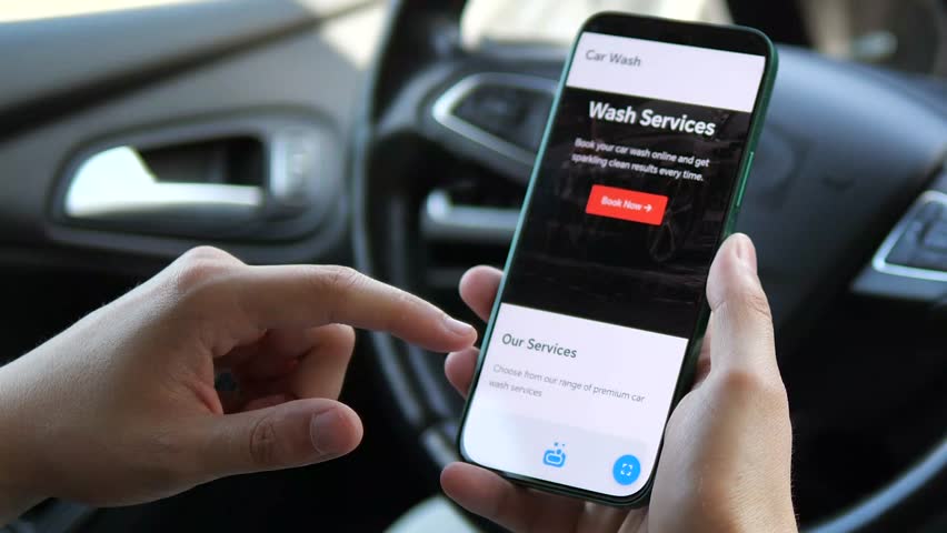 A car owner researches his options for professional car detailing directly from his drivers seat. He carefully evaluates service tiers, costs, and company information on his smartphone.