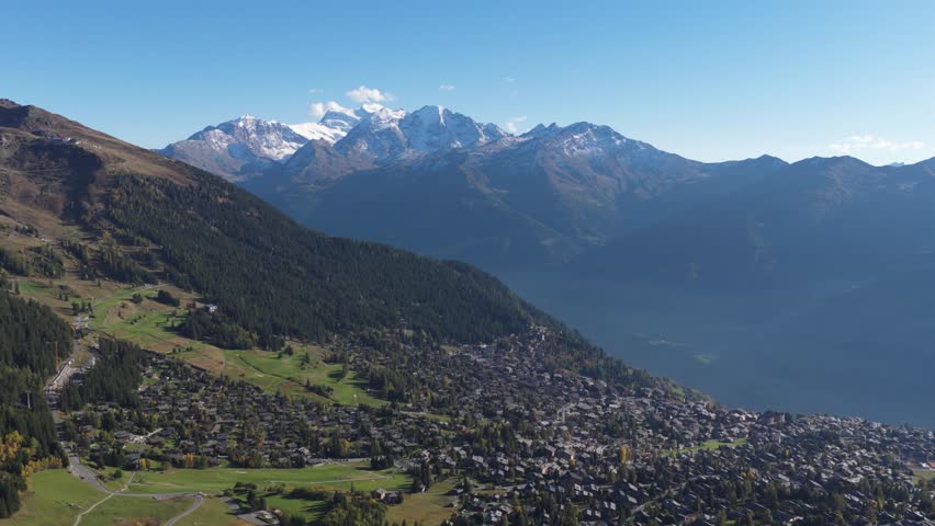 Aerial view of Verbier, a densely packed settlement nestled in a valley below snow-capped mountains with forests, Verbier, Valais, Switzerland.