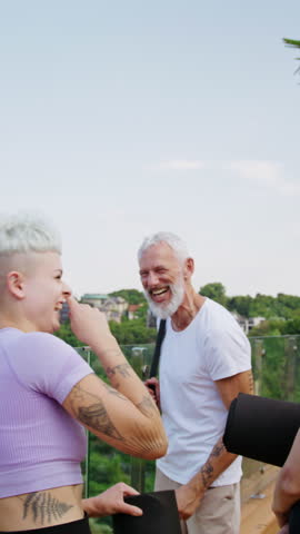 Laughing man and woman of different age give high five near Asian friend at yoga lesson in park. Multicultural sportive people radiate joy after training