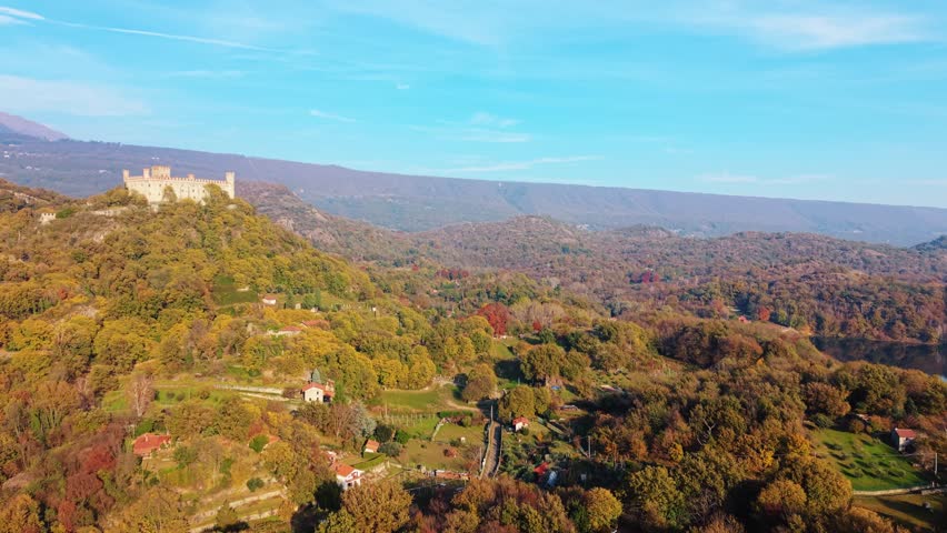 Aerial view of Castello di Montalto perched atop a hill surrounded by colorful autumn trees and distant mountains, Castello di Montalto, Piemonte, italy.