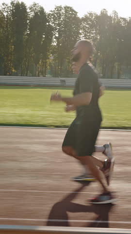 Couple of athletic people runs on stadium running track synchronously. Young African American man and biracial woman train intensively in early sunny summer morning