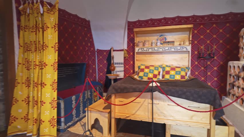Sideways tracking shot of a historical interior display in Boldogkőváralja, Hungary, featuring traditional furniture, textiles, ceramics, and ornate decorations showcasing regional craftsmanship.