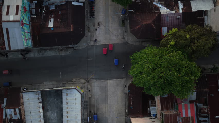 Aerial top down perspective from a tripod of a street intersection in Iquitos, Peru. Mototaxis, people and tuk tuks crossing the road in a poor district