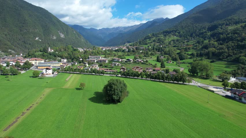 Aerial shot of Valle di Ledro showing green fields village and mountains on a clear day