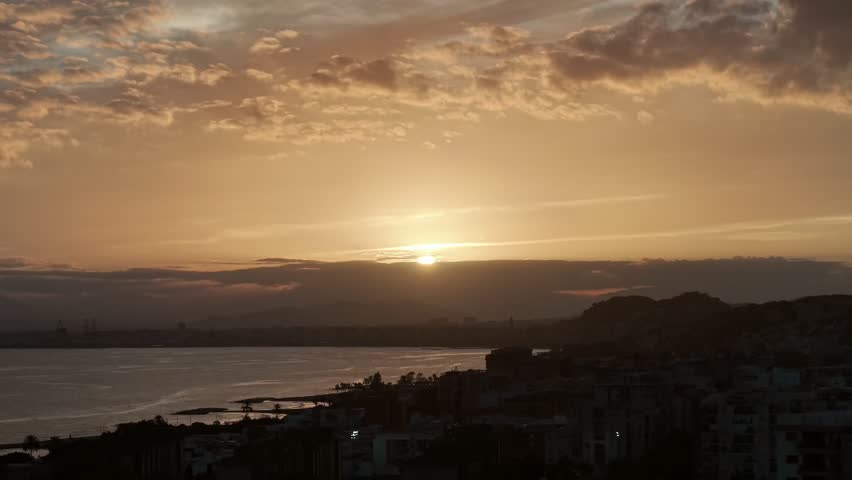 Sunset over Malaga, Spain, captured from a drone. The golden hour lights up the coastline and cityscape, offering breathtaking views of the Mediterranean and surrounding mountains.