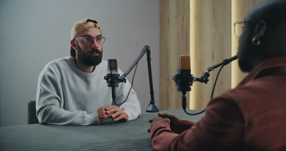 Men Having Friendly Podcast Discussion in Well Lit Studio. Two Men Professional Record Podcast, Speaking Openly and Gesturing Naturally. Concept of Creativity, and Relaxed Storytelling Vibe.