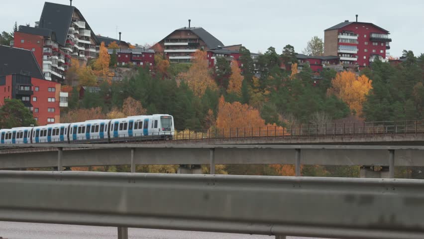 Medium shot of a Swedish subway train going on a bridge in a suburb.