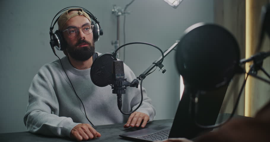 Podcast Host With Open Laptop Listening to Guest, Both Using Headphones and High End Microphones. Concept Authentic Dialogue, Creative Exchange in Modern Media Space, and Relaxed Storytelling Vibe.