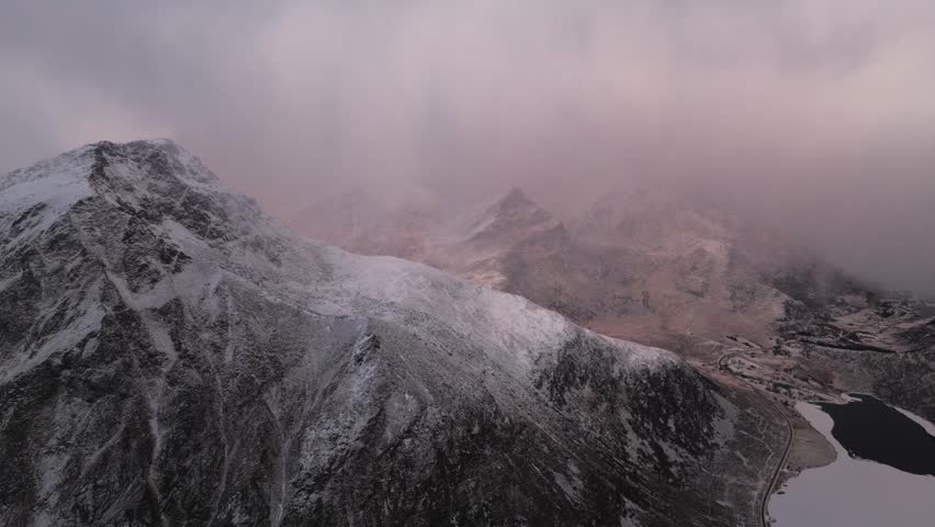 Aerial view of snow-capped mountains shrouded in mist, creating a serene yet dramatic landscape, Reine, Nordland, Norway.