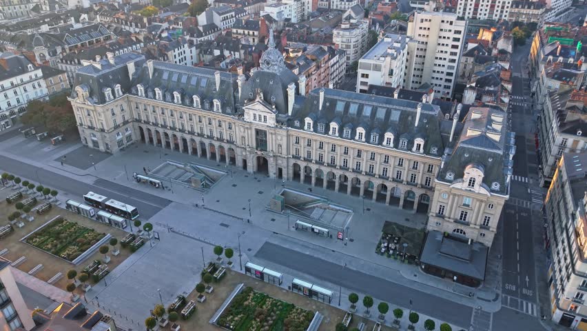 Drone advances over the Palais du Commerce in Rennes at sunrise, showing the metro entrances on Place de la République and moving toward the central dome.