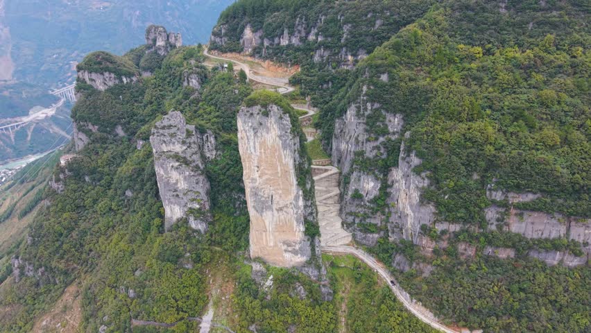 Aerial view of the steep, sheer rock formations and the zigzag road carved into the cliffside at Lingpaishi, Wuxi County, China. Captures remote natural beauty and engineering. UHD.