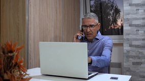 Middle-Aged Man on Phone Call While Working on Laptop - Zoom Out Shot.  During the call he pointing at the computer screen. Perfect for remote work, communication, and professional themes. - Powered by Shutterstock - Get 15% off with code: PIKWIZARD15