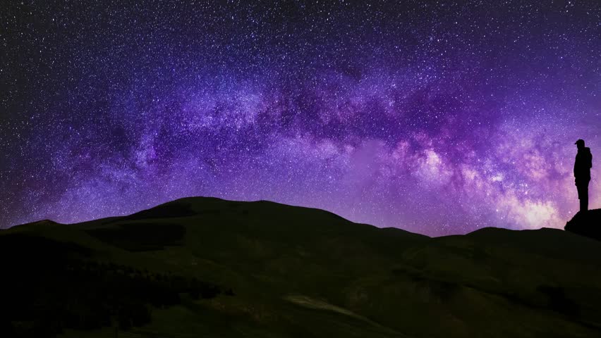 Silhouette of a man standing on a rock and looks on the bright Milky Way galaxy.