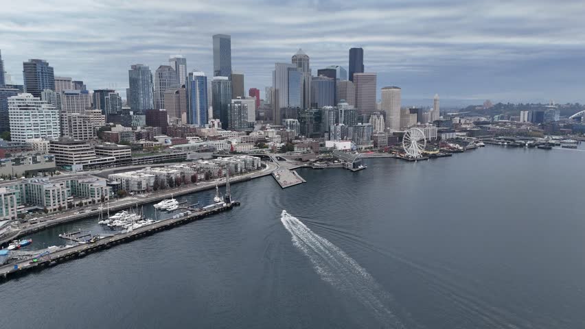 Aerial wide angle view of Seattle Waterfront with downtown skyline and Elliott Bay as a fast boat approaches the pier, Washington, United States