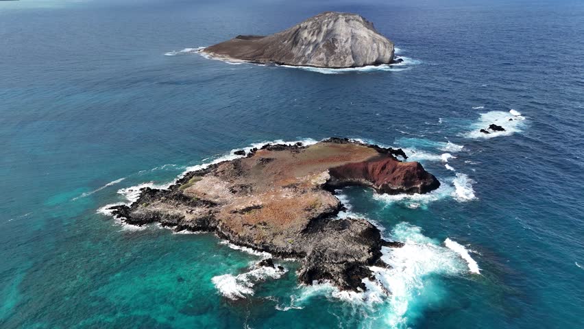 Drone above two small rocky islets off Oahu, Hawaii. Tropical ocean, dramatic coastline, blue pristine ocean water, aerial cinematic