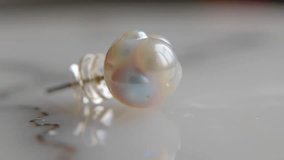 Close-up of a lustrous baroque pearl earring stud, showcasing its iridescent shimmer and unique shape on a reflective surface. Perfect for luxury jewelry promotion. - Powered by Shutterstock - Get 15% off with code: PIKWIZARD15