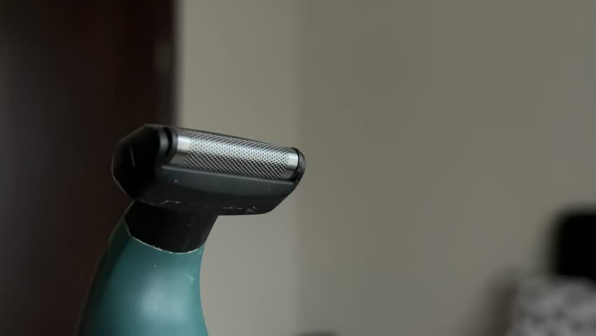 Close-up view of a vibrating electric shaver head, showing the detail of the foil and blade mechanism during operation in a bathroom, focusing on men