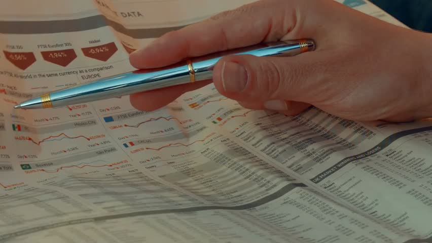 A focused investor reviews stock quotes in a financial newspaper, highlighting market analysis, decision-making, and the attentive study of economic data in a business setting.