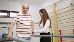 Professional female physiotherapist helping a senior male patient with walking exercises using parallel bars during a rehabilitation session - Powered by Shutterstock - Get 15% off with code: PIKWIZARD15