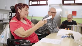 Woman with a disability in a wheelchair participating in a cooking class, reading a recipe aloud to the group. Inclusive educational workshop concept - Powered by Shutterstock - Get 15% off with code: PIKWIZARD15