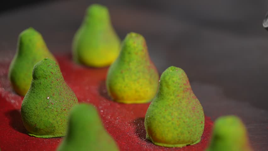A row of green pear-shaped candies are sitting on a red surface. The candies are arranged in a way that they look like a row of pears. The candies are small and green