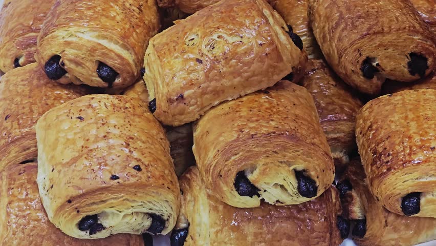 A close-up view of freshly baked, golden-brown pains au chocolat (chocolate croissants), piled high and showing the visible chocolate bars inside.