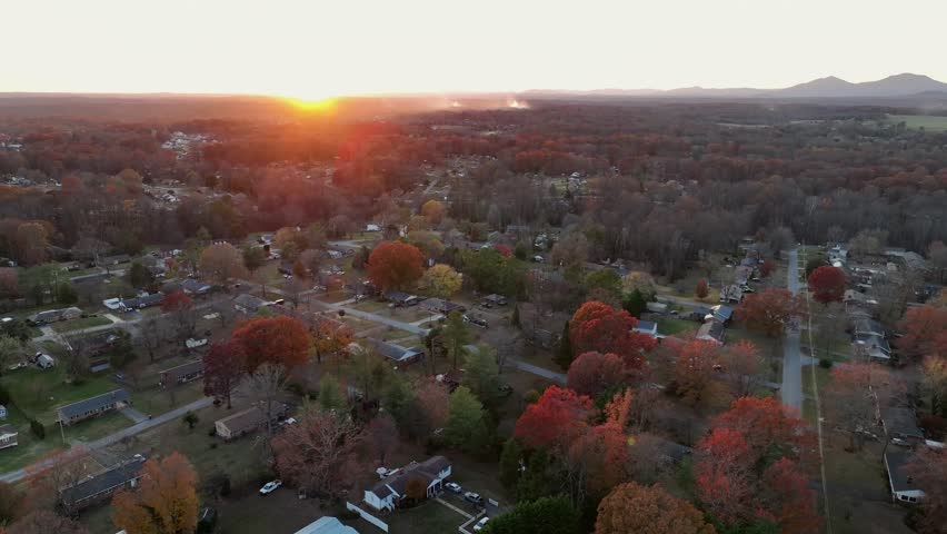 Aerial wide shot of american neighborhood with colored trees at golden sunset. Peaceful atmosphere in suburb of american town. Warm glowing light in evening.