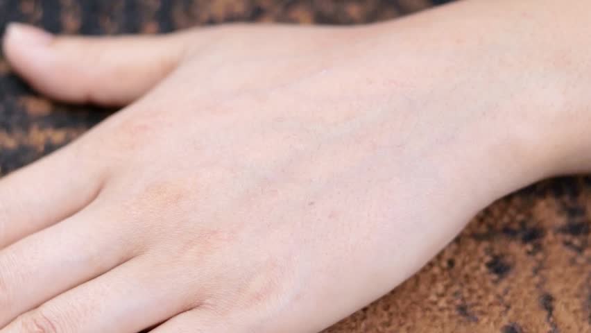 This image shows a close-up of a womans wrist as a henna tattoo artist applies a traditional mandala design with a small stick.


