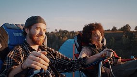 Happy mixed race hikers drink tea and observe landscape sitting near tents at sunset. Young couple relaxes after long trekking day at autumn countryside - Powered by Shutterstock - Get 15% off with code: PIKWIZARD15