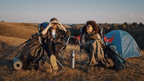 Young diverse partners share binoculars to observe landscape as sit near tents at twilight. Positive family rests after active trekking day at small camp - Powered by Shutterstock - Get 15% off with code: PIKWIZARD15