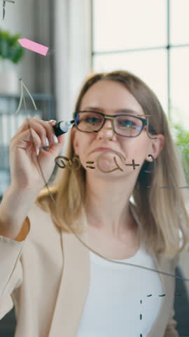 Attractive professional successful inventive man and woman of design office working together over joint project and writing schemas and reminders on glass board and sticky notes,slow motion