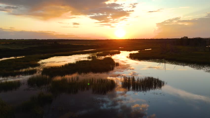 clouds reflected in a reed-covered lake at a bright orange sunset, view from a drone