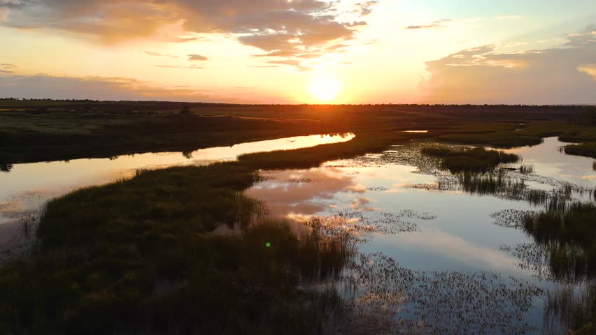 clouds reflected in a reed-covered lake at a bright orange sunset, view from a drone