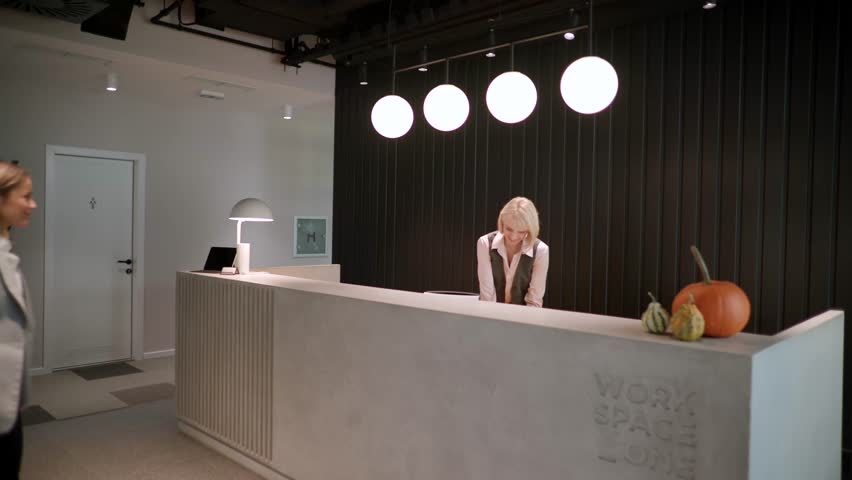 A helpful receptionist greets a guest at a sleek hotel reception, sharing smiles and warm conversation in a bright space.