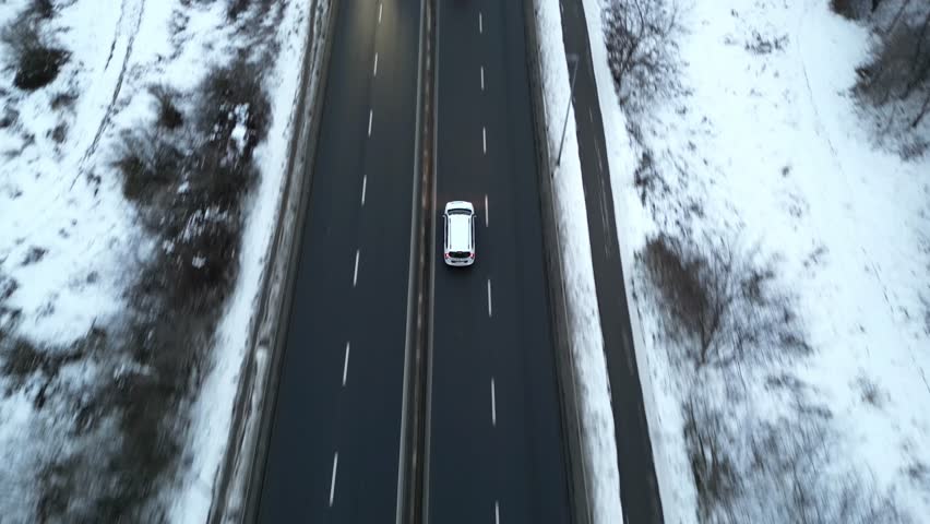 Aerial view of a cars driving along a snow-covered road, showcasing the vehicle's movement and the surrounding winter landscape, camera follows cars smoothly. Autos riding at highway at cold season