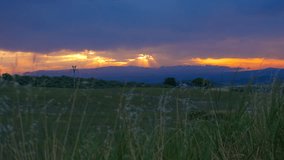 Stunning orange sunset over green countryside landscape. Beautiful orange and golden sunset creating dramatic crepuscular rays behind distant mountains, with a lush green meadow in the foreground - Powered by Shutterstock - Get 15% off with code: PIKWIZARD15