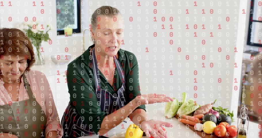 Lead cook demonstrating pepper while foreground cook slicing onion for shared salad, tablet guiding. Kitchen, group, teamwork, culinary, vegetables, cutting, knife