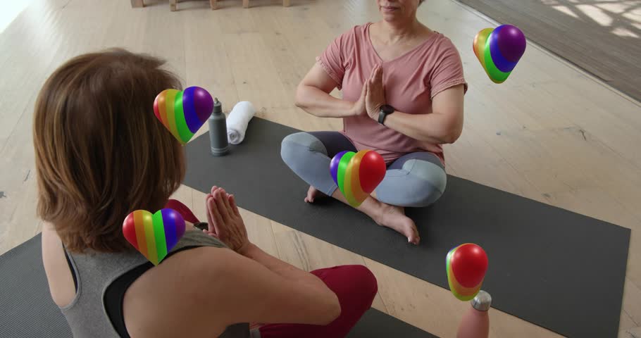Women doing yoga right shifting to mudra, left mirroring to meditate, rainbow hearts between. Duo, mats, calm, mindfulness, balance, studio, natural