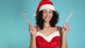 Beautiful woman in Mrs Claus costume with candy canes on light blue background. Christmas season - Powered by Shutterstock - Get 15% off with code: PIKWIZARD15