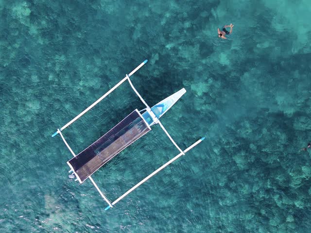 Aerial footage of a small boat floating above a vibrant snorkeling spot with clear blue water and calm tropical surroundings. Lovina, Bali.